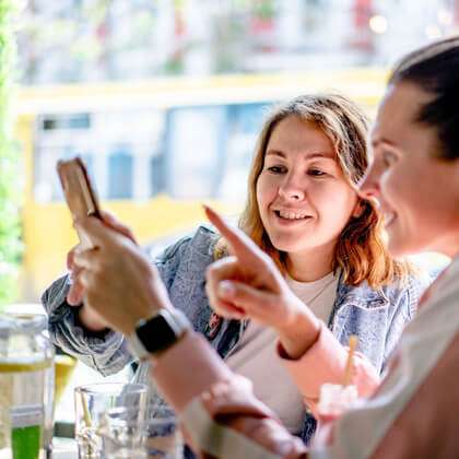 Two women at an outdoor cafe look at mobile phone